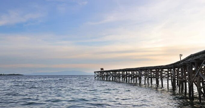 Gentle waves roll against a long wooden pier during sunset at Salat Rabia, West Papua. The glowing sky and distant islands create a calm and dreamy tropical seascape.