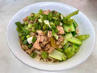 White bowl of chicken noodles topped with minced chicken and vegetables, typical Asian food