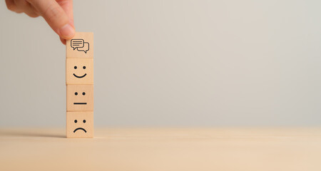 Customer feedback concept. Stacking wooden blocks with emoticon faces representing sad, neutral, and happy expressions, topped with a speech bubble icon. Customer feedback, satisfaction surveys.