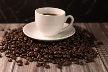 A cup of coffee and coffee beans on a dark background. Roasted coffee beans.