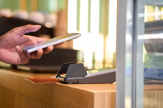 Customer paying contactless with smartphone in coffee shop