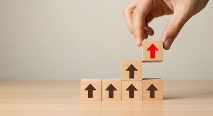 Hand Placing Red Arrow Wooden Block on Top of Stacked Blocks in a Beige Background