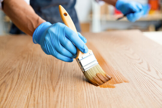 Male adult applying varnish on wooden surface with brush and blue gloves