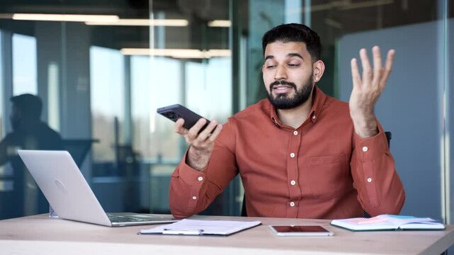 Upset male worker rejected while talking on mobile phone while sitting at the desk at the workplace in a modern business office. Unhappy businessman disappointed with negative answer or failed deal