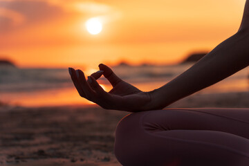 hand of a woman meditating in a yoga pose on the beach at sunset