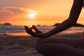 hand of a woman meditating in a yoga pose on the beach at sunset