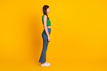 Side profile of a young fashionable woman in a green top and jeans against a vibrant yellow background, confident and stylish.