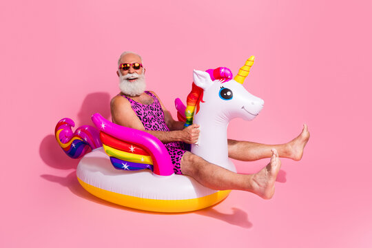Elderly man in a vibrant leopard print bodysuit celebrating summer on a unicorn float against a pink background
