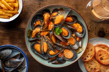 Mussels with French fries, white wine, and toasted bread, moules frites, overhead shot on a wooden table