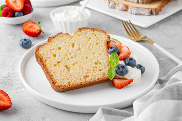 Delicious vanilla pound cake served with fresh berries and whipped cream on a gray concrete background. Selective focus, copy space.
