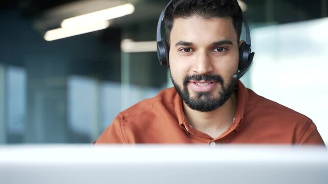 Smiling male corporate operator in headset working in customer support service on helpline telesale talking using laptop in business office. The agent of the call center advises the client. Close up