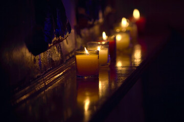 several decorative candles burning in clear glasses on a shelf in the dark