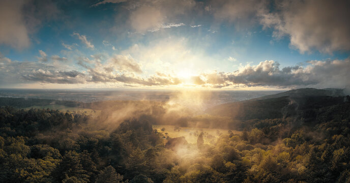 Aerial panorama of a beautiful rural landscape at sunrise, with forest and meadow, nice clouds, great light and the mist illuminated by the morning sun