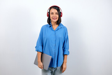 Pretty woman in a blue shirt holding a laptop and listening to music on headphones