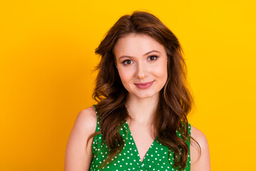 Portrait of a smiling young woman wearing a green polka-dot top against a vibrant yellow background...