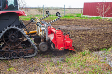 Obraz premium A tractor equipped with a red rotary cultivator actively prepares the soil in a rural field. The equipment loosens the earth, preparing it for planting and cultivation