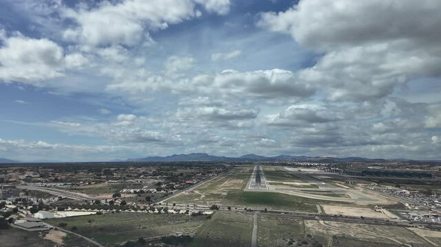 A pilot&rsquo;s perspective FPV POV in a real time approach to Alicante airport, with an aerial view of the runway under a blue sky with some cottony clouds. Aerial footage taken from a jet cockpit.