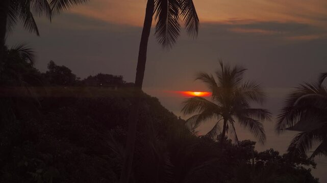 Scenic sunrise over Koh Tao, lens flare with palm trees in the foreground amd sea and hills. Thailand