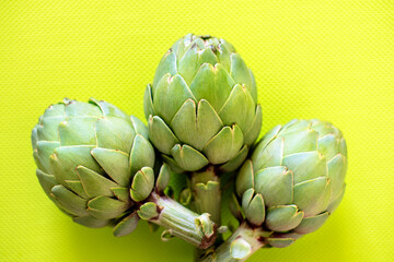 Fototapeta premium Three fresh artichokes resting on a vibrant yellow surface, showcasing their natural texture and intricate patterns. A vivid presentation of vegetables, perfect for healthy eating or cooking themes.