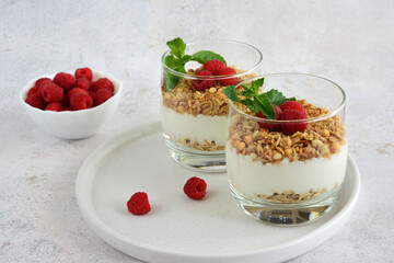 Yogurt with Granola and Fresh Raspberries in drinking glass on white tray