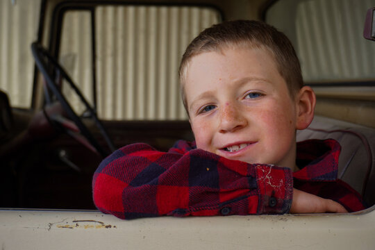 A boy resting on an elbow on the windowsill of an old truck