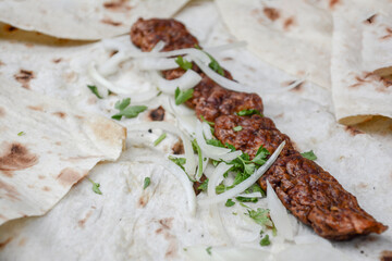 Kebab with onion and pita bread on a wooden table. Shish kebab with ketchup, herbs. Grilled kebab wrapped in pita bread. Restaurant food. Fast food with meat barbecue