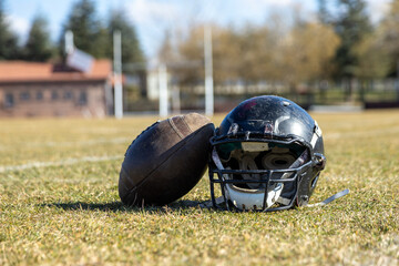 worn helmet and american football ball, worn american football helmet and football field, grass and white lines, black helmet