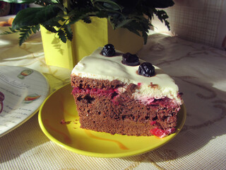 A piece of delicious chocolate cake with berry filling, topped with whipped cream and cherries on a table on a sunny day.