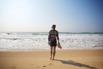 Woman walking barefoot on beach holding shoes on sunny peaceful day