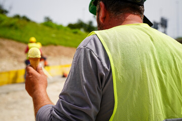 Construction worker holding an ice cream on a highway construction site, showcasing care for workers.