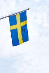 Swedish flag waving against a bright sky. The national flag of Sweden, featuring a golden cross on a blue background,  flying on a flagpole under a partly cloudy sky. Copy space