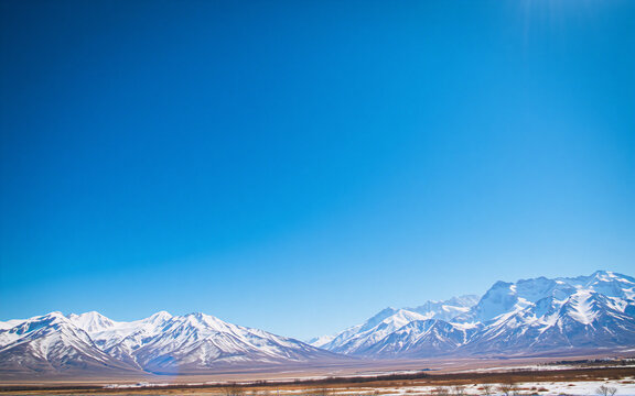 Snowy mountain range under a clear blue sky on a bright sunny day.  The landscape shows a vast expanse of nature with snow-covered peaks and a clear atmosphere.