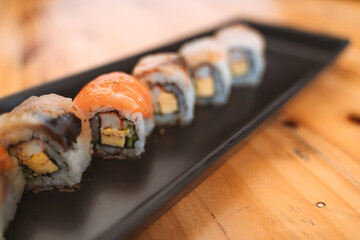 Sushi rolls with salmon, white fish, and avocado on a black rectangular plate.