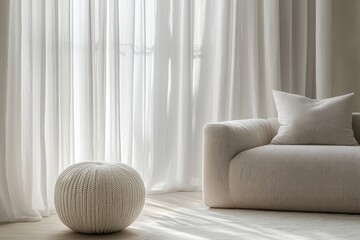 Minimalist living room with soft furnishings.  Sunlight streams through sheer curtains illuminating a modern space featuring a textured ottoman and a sculpted sofa