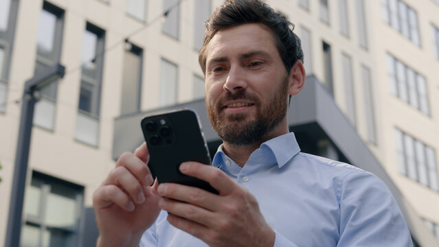 Smiling positive Caucasian middle-aged businessman business man male guy employer entrepreneur worker in city near office building using mobile phone app chatting smartphone message work job internet