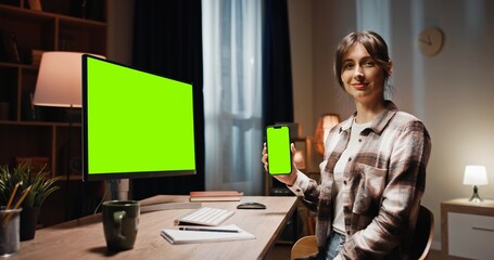 Camera sliding on side of desk where female sitting in front of computer monitor with green screen....