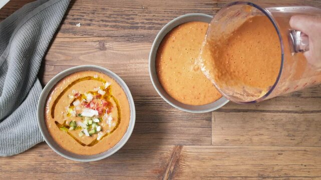 cook pour gazpacho soup in bowl and add chopped vegetables, process of making fresh cold tomato soup. food closeup, top view