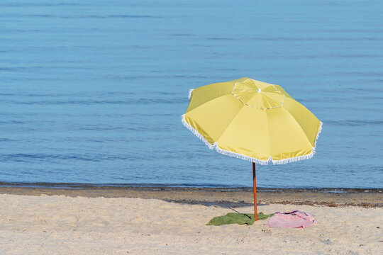 A yellow beach umberalla on a sandy beachin front of blue water
