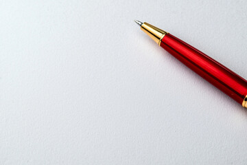 close up of red pen resting on blank white paper surface, showcasing its sleek design and shiny finish. This captures essence of writing and creativity