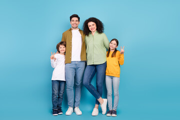 Fototapeta premium Happy family of four standing together against a blue backdrop, two children making peace signs, representing love and unity.
