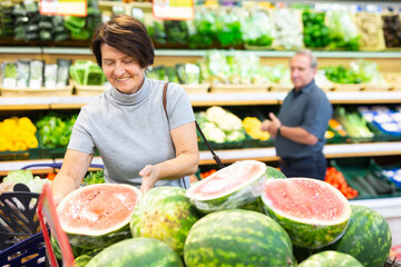 Satisfied woman chooses ripe sweet watermelon on grocery store window