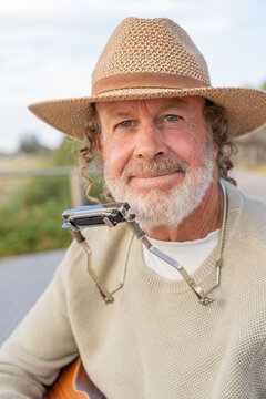 Close up of a busker wearing a hat and a harmonica around his neck smiling
