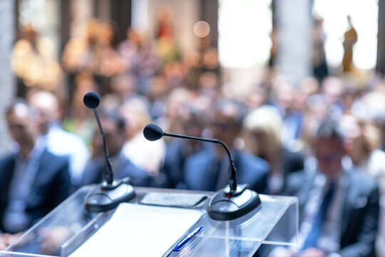 Microphones in focus, unrecognizable people in background at business conference, corporate presentation, workshop, coaching training, news conference, company meeting, public or political event