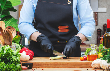 Chef cuts young garlic. Cozy kitchen with wooden table, kitchenware, vegetables, herbs and ingredients for cooking. Healthy vegan eating, culinary, recipes, food blogging