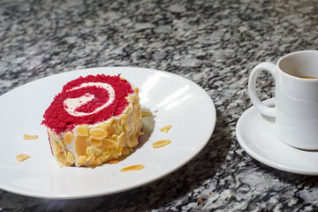 Red velvet Swiss roll with almonds and coffee. Sweet dessert on a plate, on a marble surface.