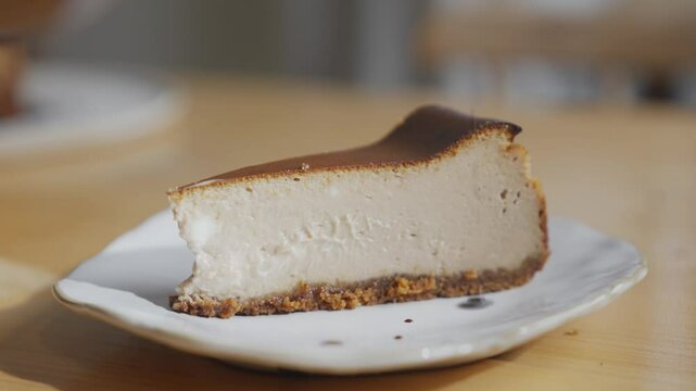 A slice of cheesecake is on a white plate. The plate is on a wooden table. The cheesecake is cut in half and is sitting on the plate
