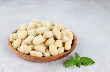 Uncooked Italian potato gnocchi on wooden plate on grey background. Top view. Copy space