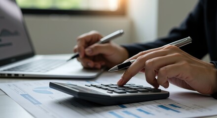 Close-up of hands using calculator and pen with financial documents and laptop. Business accounting and financial analysis concept. Tax preparation, budget planning, investment strategy.