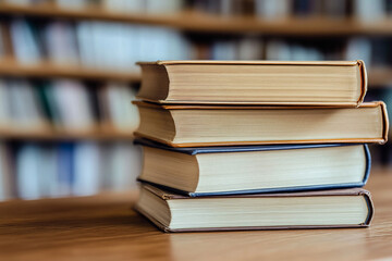 Fototapeta premium Stack of Four Hardcover Books on Wooden Table, Library Bookshelf Background
