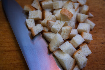 Golden brown croutons, sliced bread and knife on wooden surface, create a delicious texture and crunch. Perfect close-up of bread cubes for cooking, recipes or food background